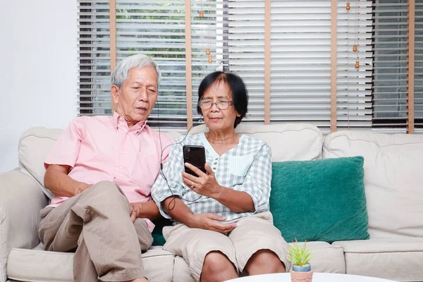 An elderly Asian couple sitting in the living room Hold a smartphone to greet children and grandchildren Via online video call