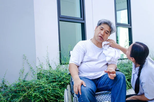 Asyalı bir adam, beyaz saçlı, hasta, felçli, yürüyemiyor, tekerlekli sandalyeye mahkum, bakması gereken bir karısı var.