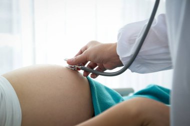Doktor, klinikteki yatakta yatan bir kadının hamileliğini kontrol etmek için çan şeklinde stetoskop kullanmış..