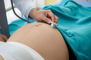 Doktor, klinikteki yatakta yatan bir kadının hamileliğini kontrol etmek için çan şeklinde stetoskop kullanmış..