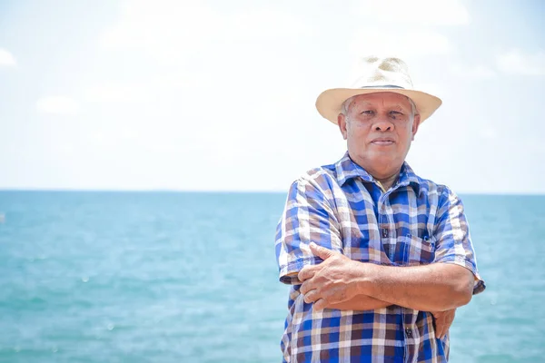 An elderly Asian man wearing a hat to visit the sea to relax