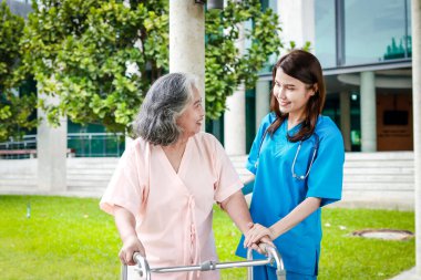 Cerrahi önlüklü Asyalı kadın doktor binanın önünde duran yaşlı kadın hastalarla ilgileniyor. Hastanelerde tıbbi hizmetler