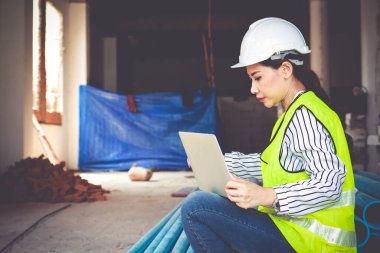 İnşaat alanında çalışan beyaz kasklı, dizüstü bilgisayarlı kadın mühendis. İnşaat endüstrisi konsepti