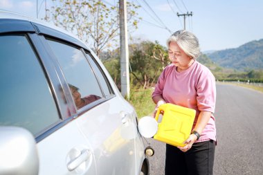 Yaşlı bir kadın benzini bittiği için yolda bir arabaya yakıt dolduruyor. Enerji konsepti. Emeklilik seyahati. ulaşım