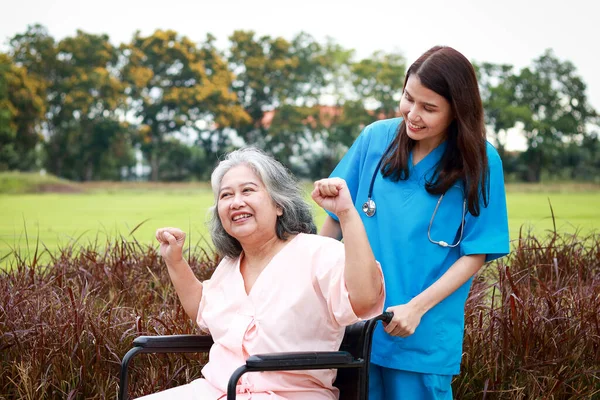 Asyalı kadın doktor, tekerlekli sandalyedeki yaşlı bir hastayı temiz hava alması için dışarı çıkardı. İkisi de mutlu bir şekilde gülümsedi. Yaşlı bir bakıcı. Sağlık, sağlık sigortası