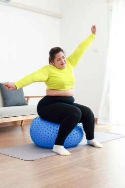 Evde egzersiz yapan şişman Asyalı kadın yoga topuna oturuyor. Sağlık sigortası, kilo kaybı. spor konsepti