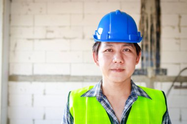 Portrait of Asian male system engineer wearing blue helmet on building construction site. Construction industry business concept. copy space