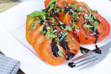 Bir tabak domates, doğranmış fesleğen ve balzamik sirke.