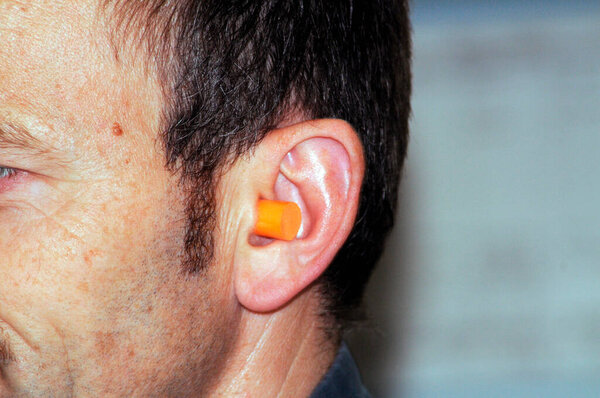 middle aged man wearing an orange earplug for hearing protection