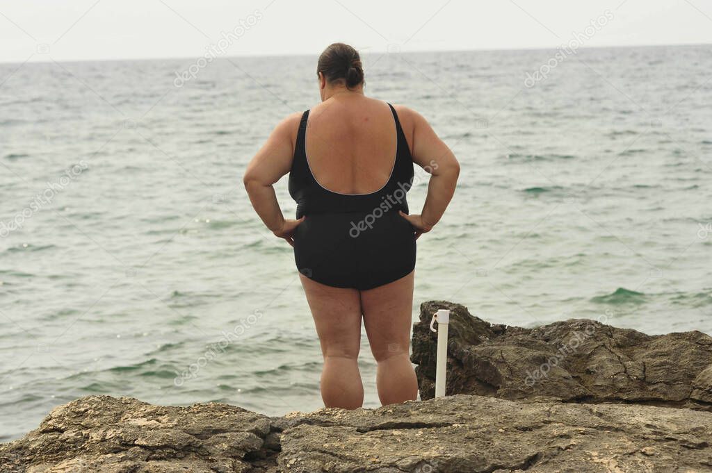 Obese woman in a black swimsuit standing at the beach