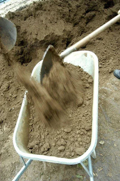 shovel filling a wheelbarrow with sand at the construction site