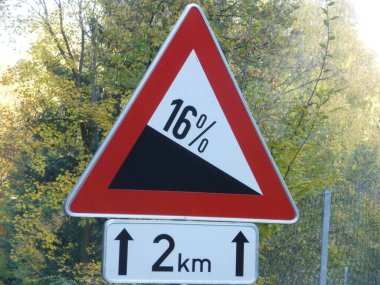 Trafik işareti gradyanı% 16, dik yol önümüzde, kırmızı üçgen, arka planda ağaç