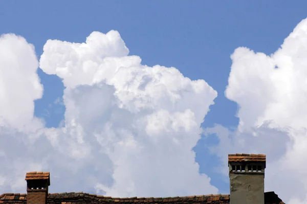clouds in the blue sky, big white cloud formation and house roof with chimneys