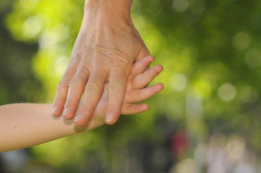 El ele tutuşan bir anne ve çocuk, bulanık yeşil bir arka plan.