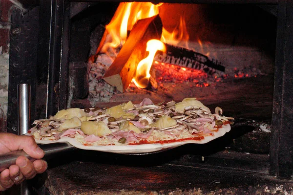 pizza chef shoves the pizza into the hot wood oven