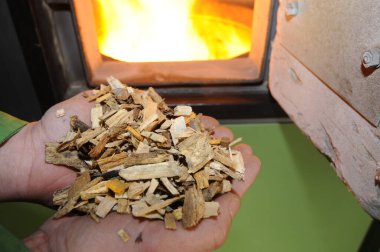 holding wood chips in hands, burning fire in oven in the back, heating with wood chips at home clipart