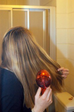 young woman blow drying her long blonde hair with a red hair dryer clipart