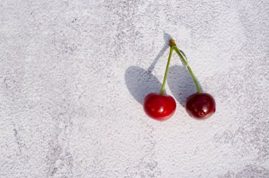 Gri arka planda iki kiraz yatar. Bir dalda iki olgun vişne. Meyveli arkaplan