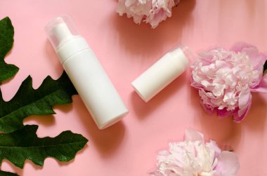 Pembe arka planda iki farklı boyutta çiçek ve yapraklı iki beyaz şişe. Güzellik konsepti