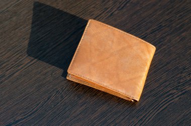 Kahverengi ahşap bir masada açık kahverengi bir çanta. Cüzdanında güneş ışınları parlıyor.