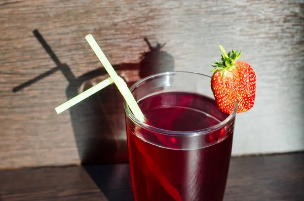 A glass of strawberry juice on a brown wooden table. The sun\'s rays shine on a glass of juice. Natural strawberry juice