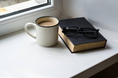 Kahve, kitap ve bardaklarla dolu beyaz bardak pencere eşiğinde duruyor. Eğitim ve Rahatlama Konsepti