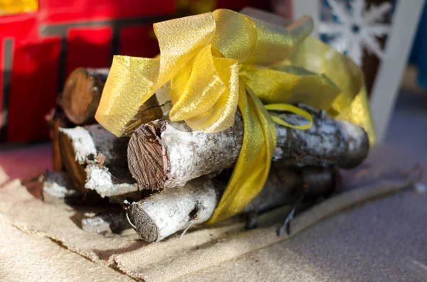 Березовые дрова лежат рядом с искусственным камином, завязанным золотой лентой. Поздравительная открытка. Рождественские каникулы. — стоковое фото