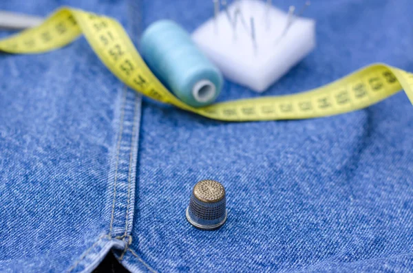 There are sewing supplies on top of the denim items. A centimeter, threads, pins and a thimble lie on things. Cutting and sewing concept.