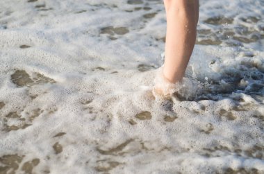 Kadınların bacakları deniz dalgalarıyla kaplıdır. Ayaklar suyun içinde, yakın plan..