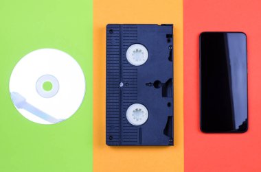Çok renkli bir arkaplanda bilgisayar diski, video kaset ve akıllı telefon.