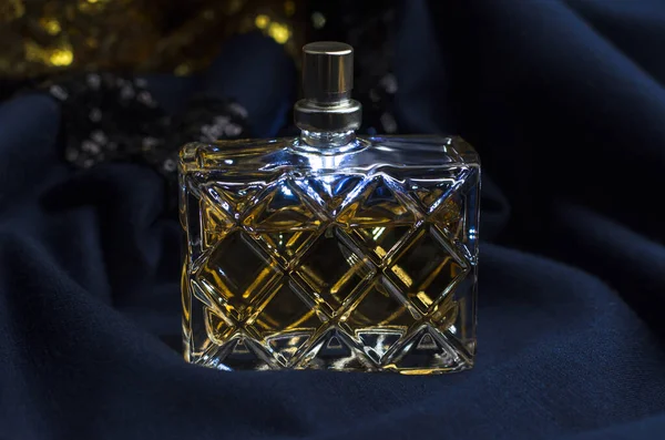 Women\'s perfume on a blue fabric with golden sequins.