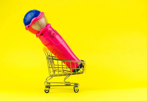 黄色背景购物车中的粉色玩具话筒 — 图库照片
