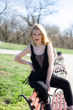 Parktaki bankta bir kız. Siyah elbiseli sarışın. Siyah elbiseli güzel bir sarışın. Dudaklarında kırmızı ruj var.