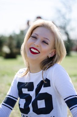 Güzel kız gülümsüyor. Dudaklarında kırmızı ruj var. Doğadaki kız. Sarışın.