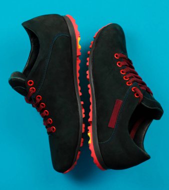 Mavi arka planda kırmızı bağcıklı siyah bir çift spor ayakkabı. Modaya uygun gençlik ayakkabıları