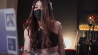Siyah koruyucu maskeli genç Asyalı kadın DJ gece kulübünde karıştırma konsolunun yanında duruyor, maskeli Asyalı kadın covid-19 sırasında müzik karıştırıyor, canlı performans, karantina karşıtı, covid dj
