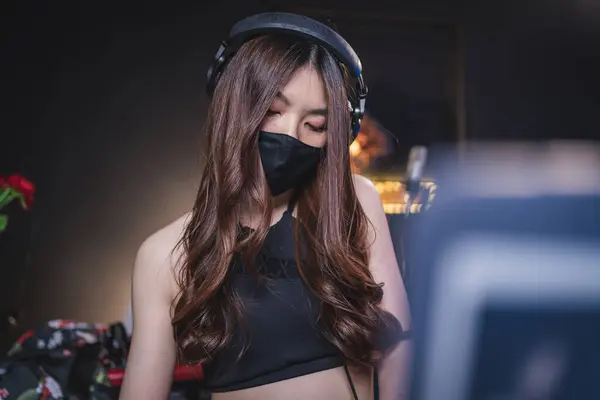 female dj in black protective mask enjoying her music, standing in nightclub,covid dj, electronic music, laptop audio software, live performance, anti-quarantine, covid dj