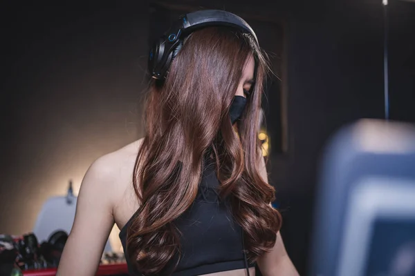 Siyah maskeli genç Asyalı seksi bayan DJ gece kulübünde karıştırma konsolunda, Asyalı kadın online siber canlı müzik klüpte covid-19 sırasında canlı performans, sosyal mesafeli covid dj