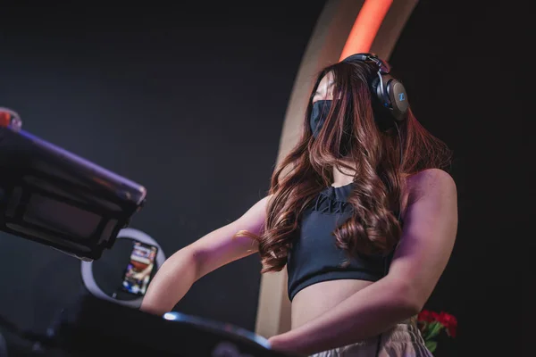 Asya Dj 'i siyah maske takıyor dizüstü bilgisayarda ve pikapta müzik çalıyor, maskeli Asyalı kadın Covid-19 kulübündeki müziği ayarlıyor, canlı yayın performansı, ritmi yükseltiyor.
