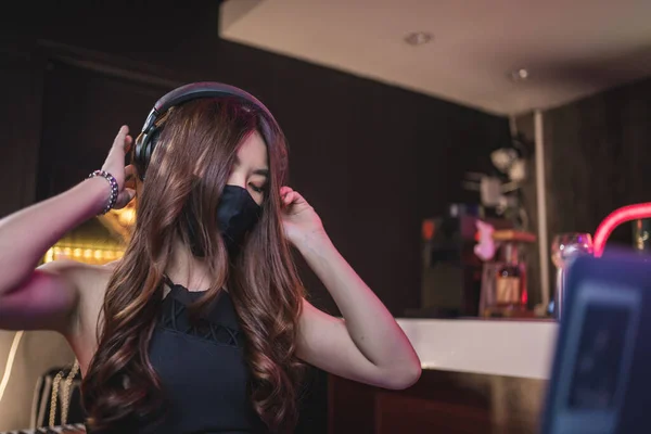Seksi siyah spor sütyenli Asyalı kadın DJ dizüstü bilgisayarla müziği akort ediyor, gece kulübü karantinasında Asyalı kadın covid-19, gece kulübü endüstrisi, beat culture, siber yaşam tarzı, kulaklık tasarımı