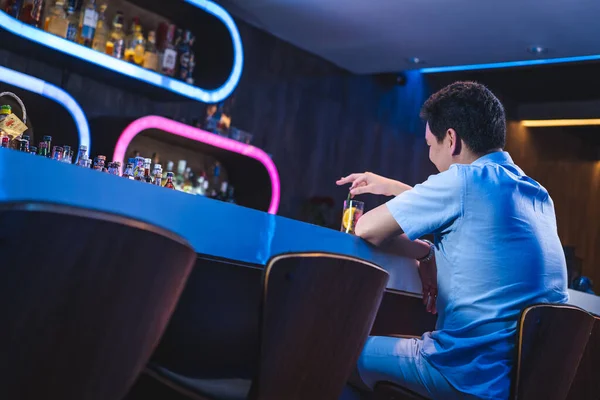 Arkadan bakıldığında Asyalı erkek mavi gömlekli beyaz alkol barında tek başına oturuyor, erkek arkadaşını bekliyor, bira ve bistro, içecek endüstrisi, mavi renkli LED ışığı, özel yaşam ayrıcalığı