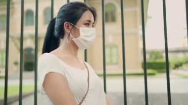 Beyaz koruyucu maske takan Asyalı genç bir kadının portresi, covid-19 Corona virüsü, sağlık sigortası, yeni normal yaşam tarzı, gün ışığı, kameraya bakan model, sağlık ve güvenlik kavramı