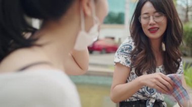 İki Asyalı bayan arkadaş, parktaki kovid-19 sırasında birbirleriyle konuşuyorlar. Yeni normal yaşam tarzlarını karantinaya alıyorlar. İki kız arkadaş arasındaki samimi konuşma neşe dolu gülümseme iletişimini tartışıyor.