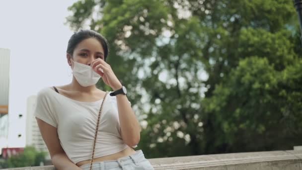 亚洲女人戴着防护面具站在室外 亚洲19世纪大流行 健康的生活方式 新的正常社交距离 下午的阳光 城市背景 亚洲女人戴着医疗面具 — 图库视频影像