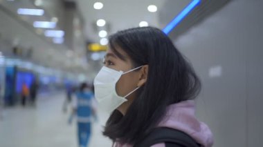 Asyalı kadın havalimanı uçuşunda maske takıyor kalkış zamanı tablosu, havaalanı kontrolünde karşı terminal, umumi alan virüsü covid-19 salgını, yeni normal yaşam sosyal mesafesi