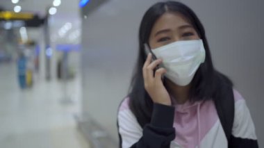 Asyalı genç kadın koruyucu maske takıyor. Telefon havaalanı, havaalanı terminali, virüslü covid-19 salgınından güvenli seyahat, yeni normal sosyal mesafe konsepti, yavaş çekim.