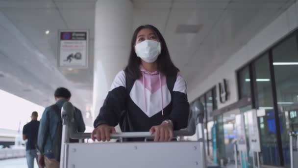 ターミナル外の空港で荷物カートを押す保護マスクのアジアの女性 コロナウイルスCovid 19パンデミック 新しい正常な社会的距離 空港ターミナル外タクシーを待っている女性 — ストック動画