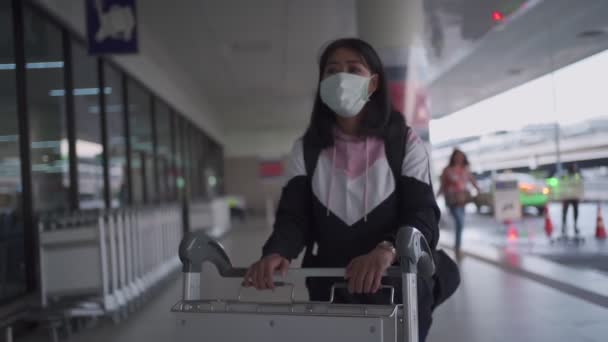 ターミナル外の空港で荷物カートを押す保護マスクのアジアの女性 コロナウイルスCovid 19パンデミック 新しい正常な社会的距離 空港ターミナル外タクシーを待っている女性 — ストック動画