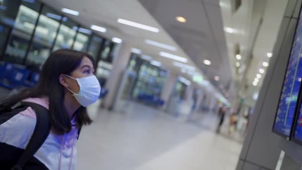 亚洲女性乘客戴着防护口罩站在候机台目视出发时间 在机场候机楼 在离开家乡时出现了Covid 19大流行病 新的正常航班时间安排 — 图库视频影像