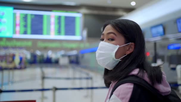 亚洲妇女戴着医疗面罩站在机场航班上 有登机时间表 机场检查柜台终端 公共场所病毒共19种流行 新的正常生活与社会保持距离 — 图库视频影像